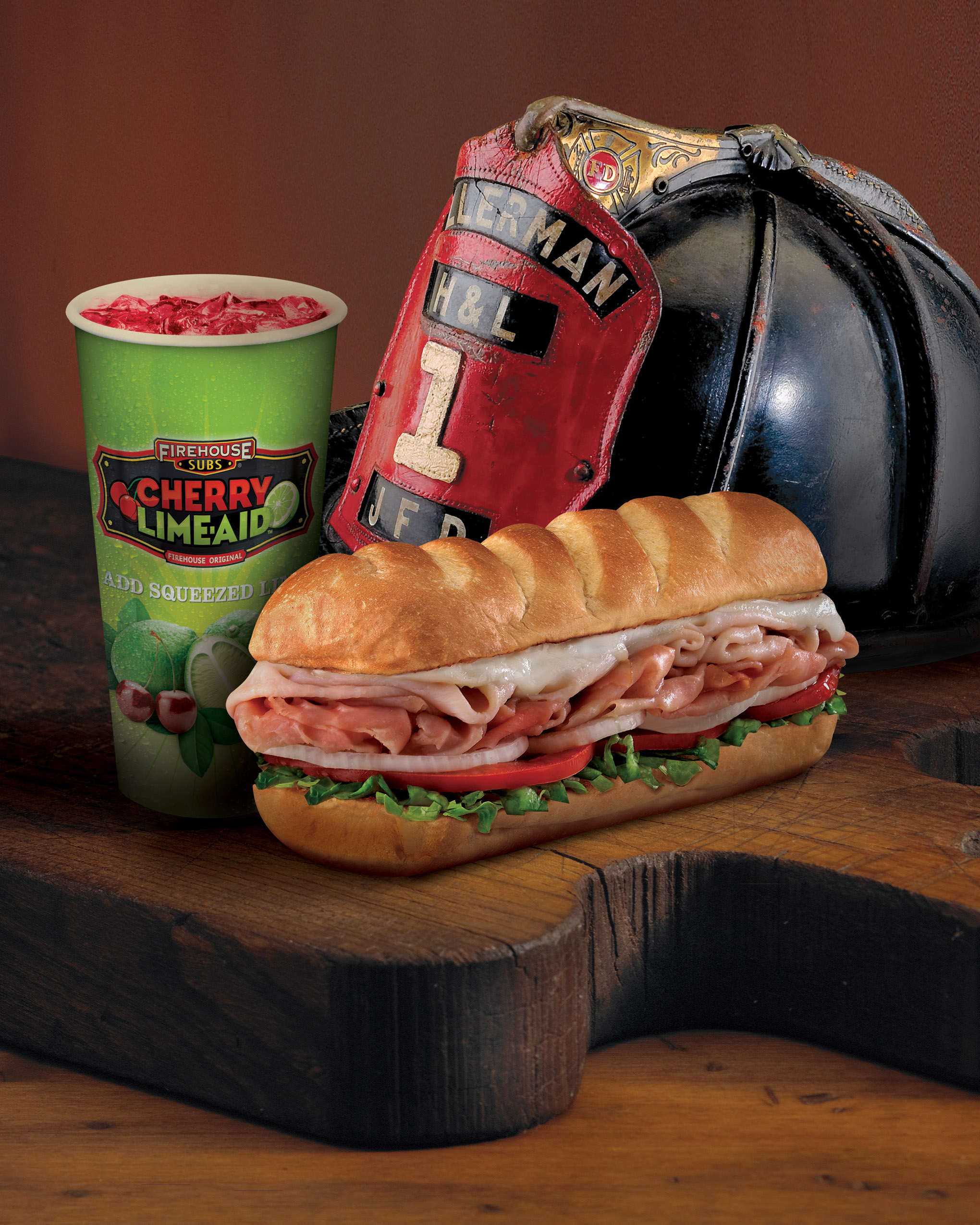 A Firehouse sub with a cherry lime-aid and a firefighter helmet, on wood
