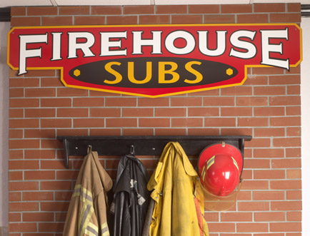 Brick wall with the logo and firefighter gear hanging off hooks